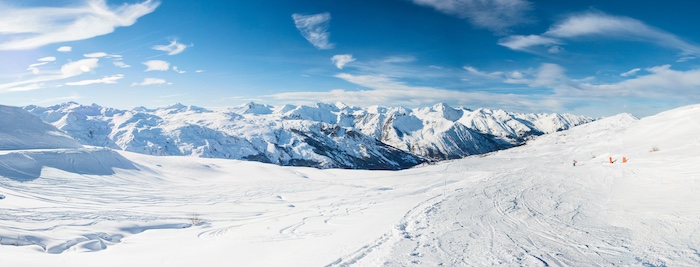 Panoramic view down snow covered valley in alpine mountain range on blue sky background